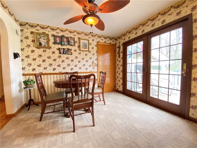 carpeted dining space with a ceiling fan, visible vents, arched walkways, baseboards, and wallpapered walls