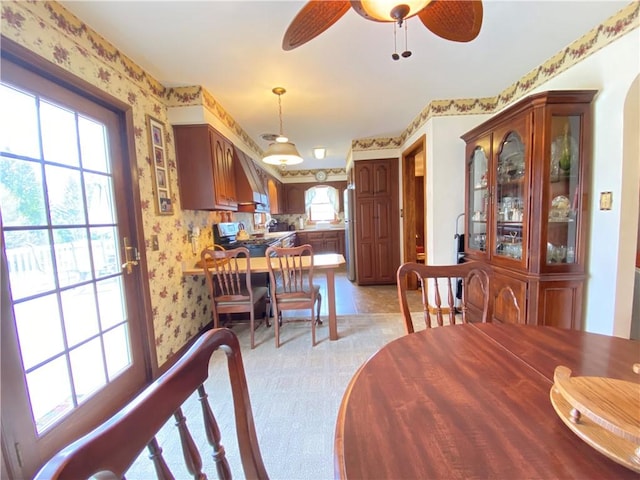 dining area featuring a ceiling fan, light carpet, and wallpapered walls