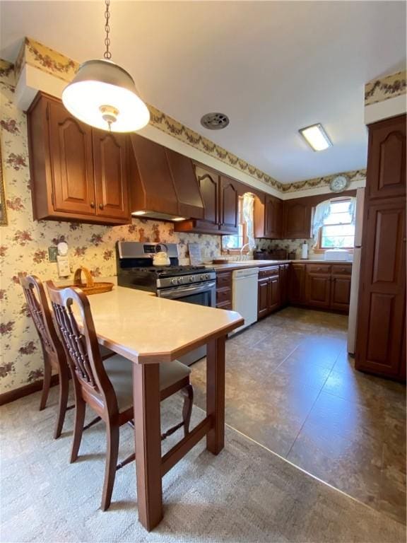 kitchen with white dishwasher, stainless steel gas range oven, a peninsula, wallpapered walls, and custom exhaust hood
