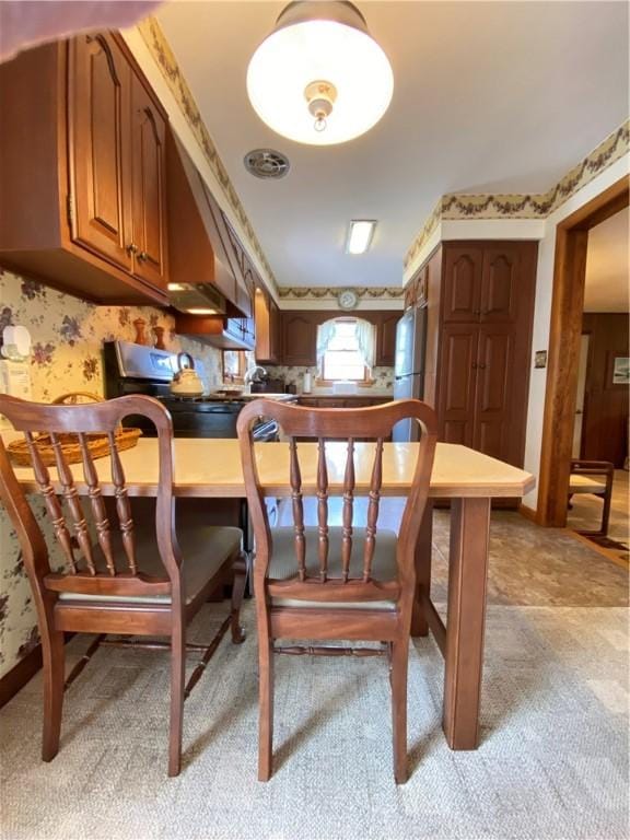 interior space featuring brown cabinets, freestanding refrigerator, a peninsula, light carpet, and wallpapered walls