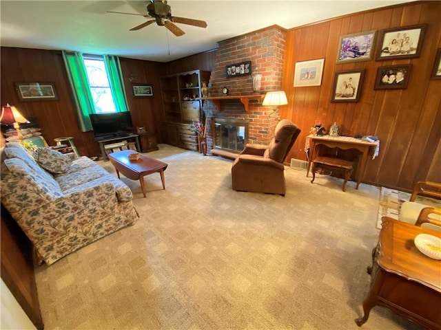 carpeted living area with wood walls, a brick fireplace, and ceiling fan