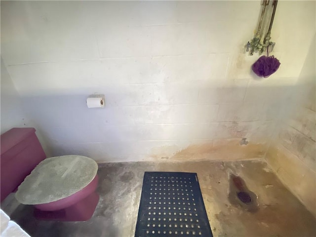 bathroom featuring toilet and concrete block wall