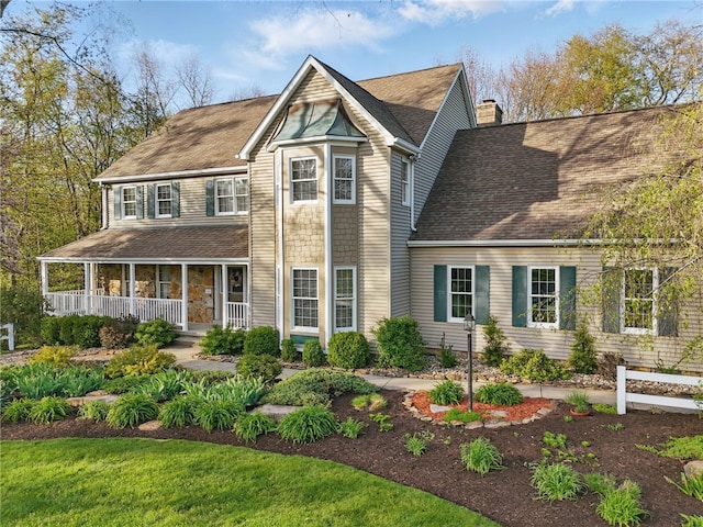 view of front of home featuring covered porch, a chimney, and a shingled roof
