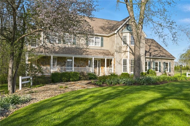 view of front of house featuring a porch, roof with shingles, stone siding, and a front lawn
