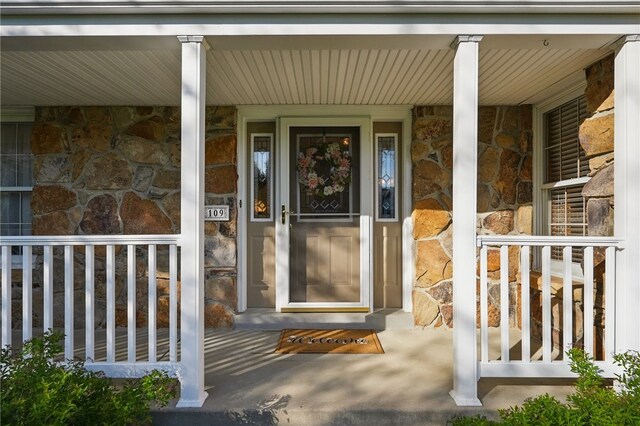 doorway to property with a porch and stone siding
