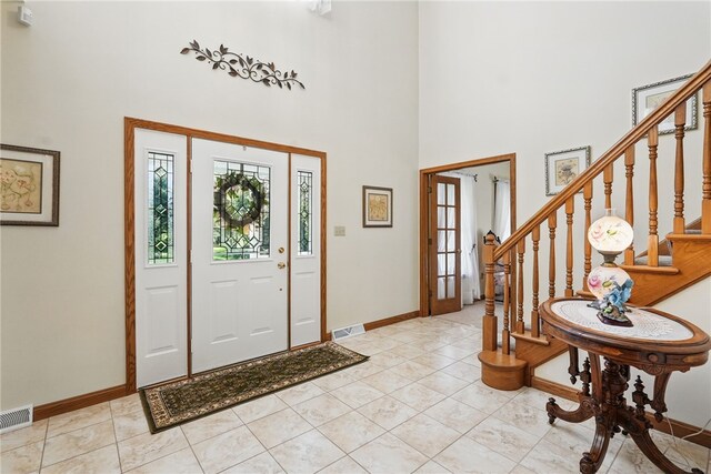entrance foyer featuring visible vents, baseboards, a towering ceiling, and stairway