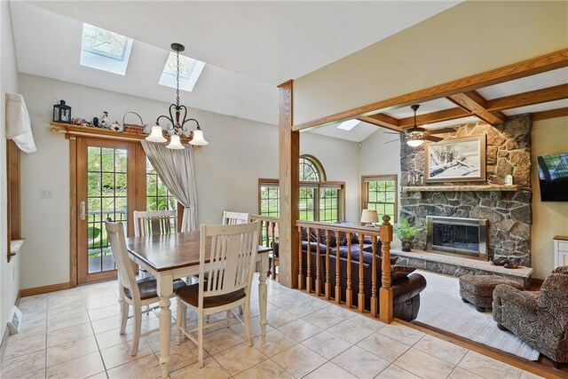 tiled dining space with baseboards, ceiling fan with notable chandelier, lofted ceiling with skylight, and a stone fireplace