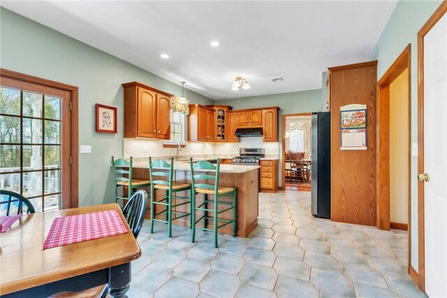 204 Salt Works Rd, Lancaster Twp, PA 16037 - kitchen featuring appliances with stainless steel finishes, under cabinet range hood, brown cabinets, backsplash, and a breakfast bar