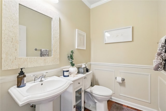bathroom with crown molding, wainscoting, a decorative wall, toilet, and a sink