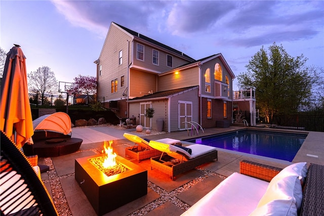 pool at dusk featuring a fire pit, fence, a patio, a fenced in pool, and an outbuilding