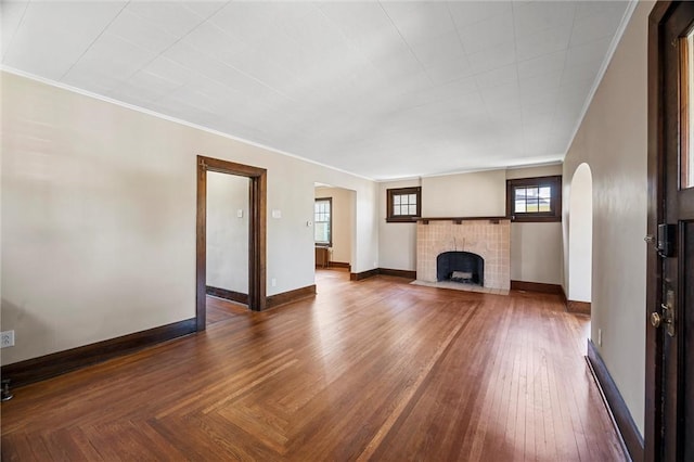 unfurnished living room featuring crown molding, arched walkways, a tiled fireplace, and baseboards