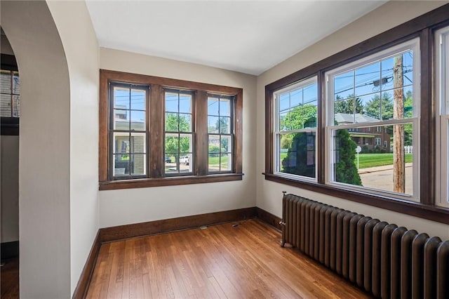 empty room featuring baseboards, arched walkways, radiator heating unit, and hardwood / wood-style floors