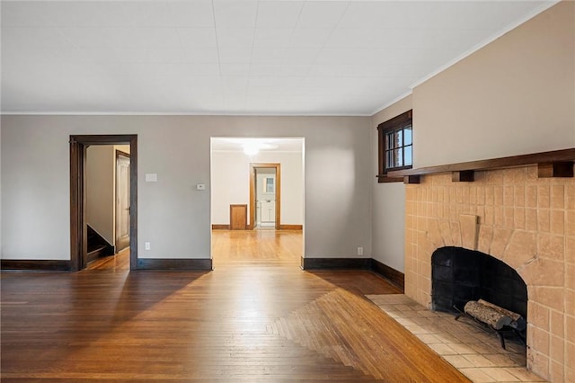 unfurnished living room with a tiled fireplace, baseboards, stairs, and wood finished floors