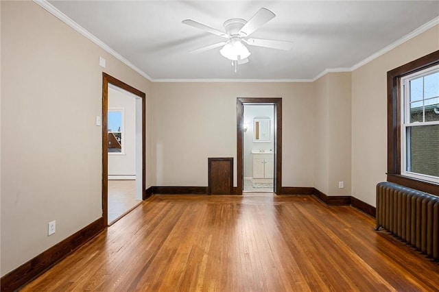spare room with crown molding, radiator, baseboards, and wood finished floors