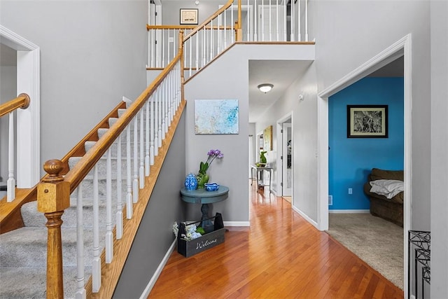 stairs featuring baseboards, hardwood / wood-style flooring, and a towering ceiling
