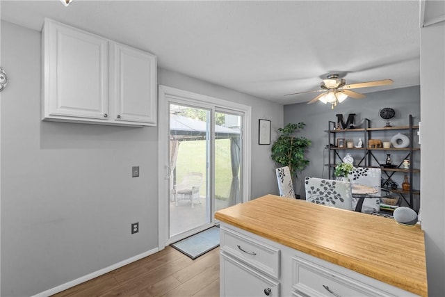 kitchen with light wood finished floors, light countertops, white cabinetry, baseboards, and a ceiling fan