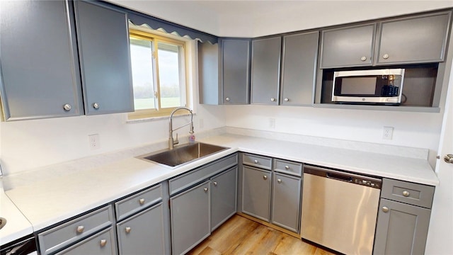 kitchen featuring light countertops, stainless steel appliances, gray cabinetry, and a sink