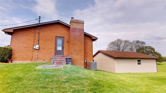 rear view of house with central AC, brick siding, entry steps, a chimney, and a lawn