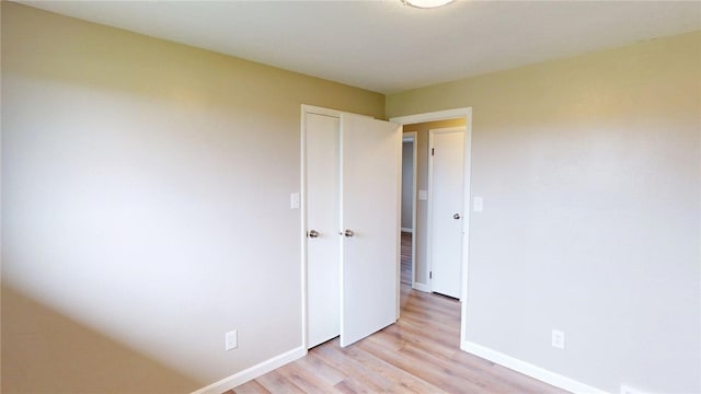 unfurnished bedroom featuring baseboards, light wood finished floors, and a closet