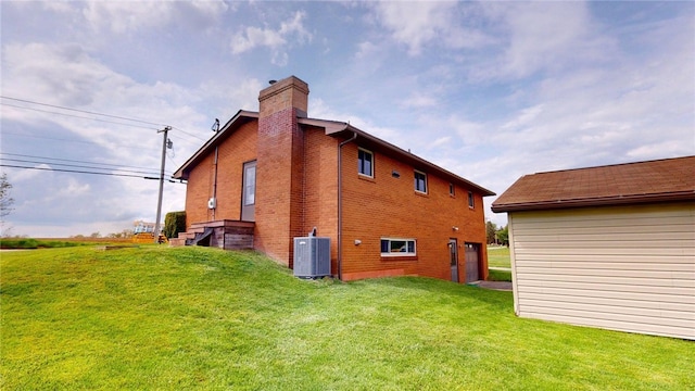 rear view of house featuring a chimney, a lawn, a garage, central air condition unit, and brick siding