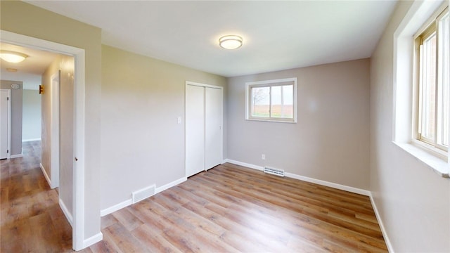 unfurnished bedroom featuring baseboards, visible vents, light wood finished floors, and a closet