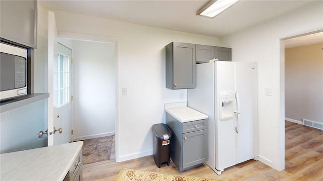 kitchen featuring visible vents, white refrigerator with ice dispenser, gray cabinetry, light countertops, and light wood finished floors