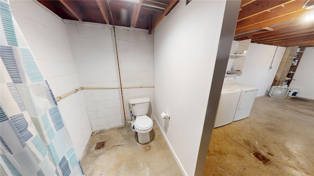 bathroom featuring concrete block wall, concrete flooring, washing machine and dryer, and toilet