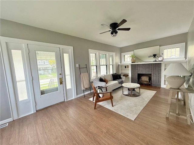 living area featuring a ceiling fan, wood finished floors, a healthy amount of sunlight, and a fireplace