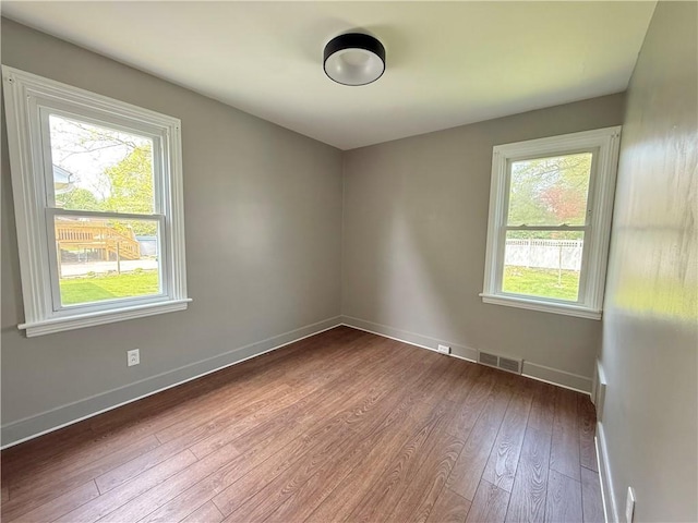 empty room with baseboards, wood-type flooring, and visible vents