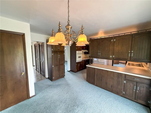 kitchen with dark brown cabinetry, light colored carpet, a chandelier, decorative light fixtures, and white oven
