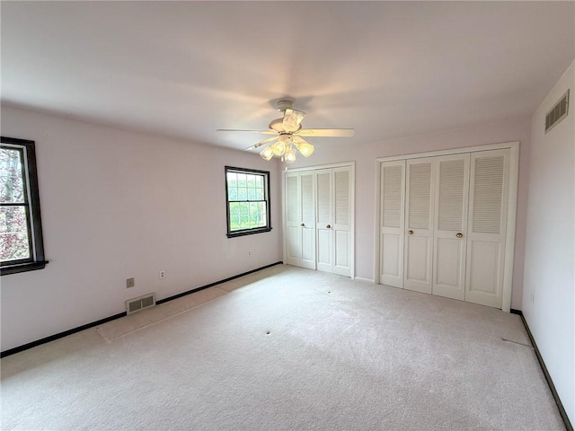 unfurnished bedroom with light colored carpet, multiple closets, visible vents, and a ceiling fan