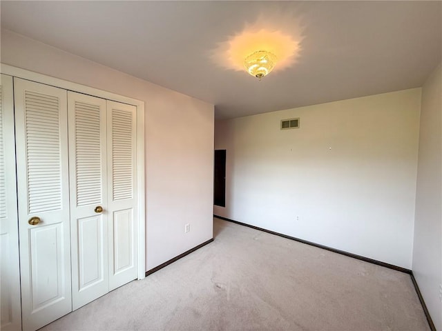 unfurnished bedroom featuring baseboards, light colored carpet, visible vents, and a closet