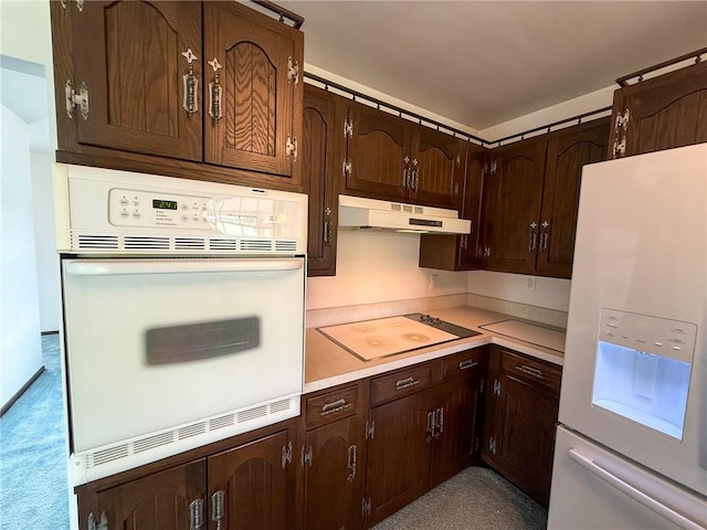 kitchen with light countertops, under cabinet range hood, white appliances, and dark brown cabinets