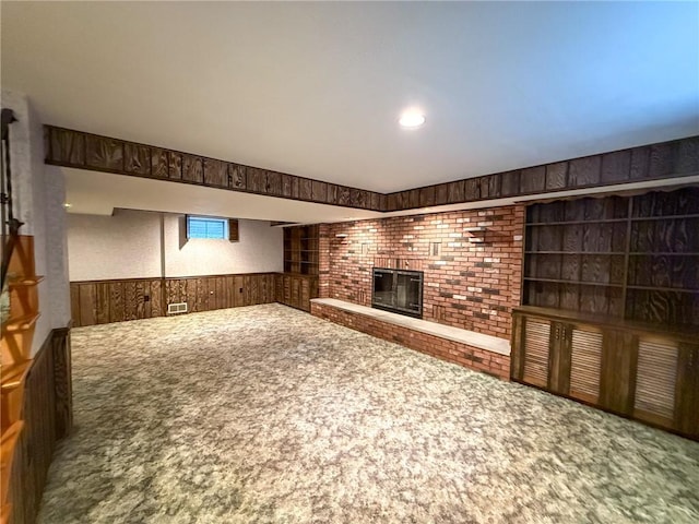 unfurnished living room with carpet floors, wood walls, visible vents, a brick fireplace, and a wainscoted wall