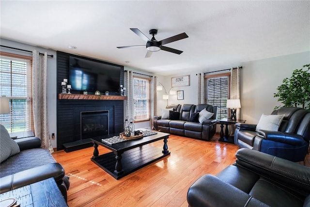 living room featuring a brick fireplace, a ceiling fan, and light wood-type flooring