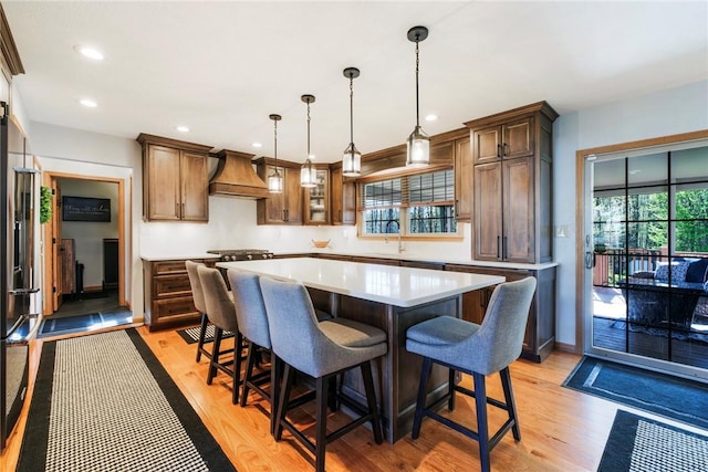 kitchen with light wood finished floors, a breakfast bar area, light countertops, custom range hood, and a kitchen island