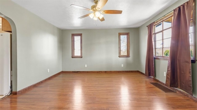 empty room with visible vents, wood finished floors, baseboards, ceiling fan, and arched walkways