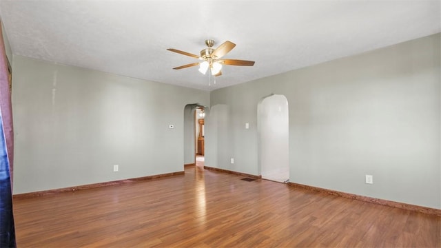unfurnished room featuring visible vents, a ceiling fan, wood finished floors, baseboards, and arched walkways