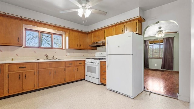kitchen with a ceiling fan, under cabinet range hood, brown cabinets, and white appliances