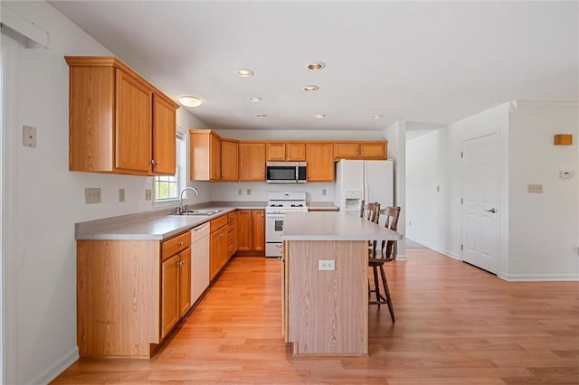 kitchen with a sink, a breakfast bar area, white appliances, and light wood-style flooring