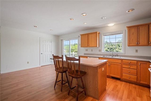 kitchen featuring a kitchen bar, a center island, a sink, light countertops, and light wood-style floors