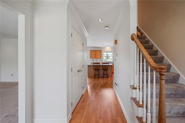 hallway featuring stairs, crown molding, baseboards, and light wood finished floors