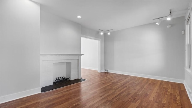 unfurnished living room featuring a fireplace with flush hearth, baseboards, rail lighting, and wood finished floors