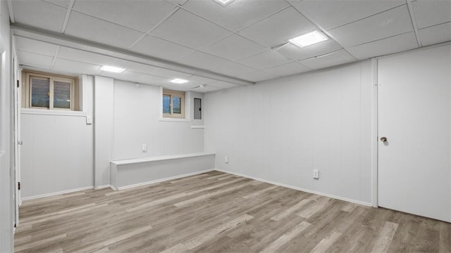 finished below grade area featuring a paneled ceiling, baseboards, wood finished floors, and electric panel