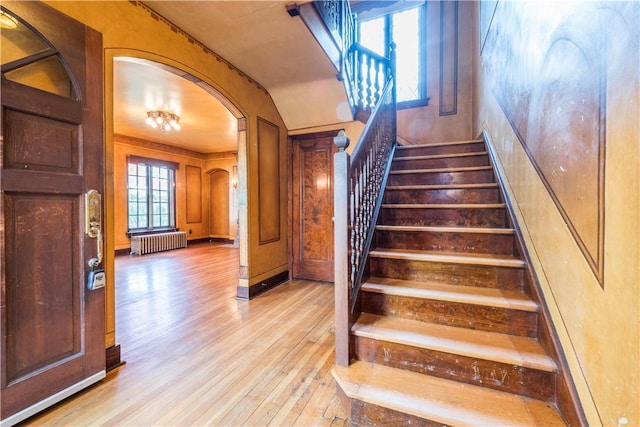 stairs with radiator, arched walkways, and wood finished floors