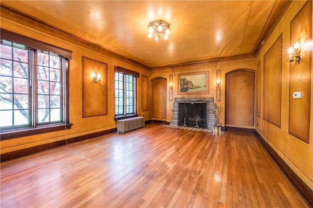 unfurnished living room with ornamental molding, a fireplace, radiator heating unit, light wood-type flooring, and arched walkways