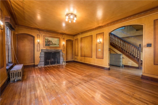 unfurnished living room with wood-type flooring, crown molding, a fireplace with flush hearth, stairs, and arched walkways