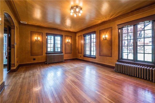 unfurnished room with crown molding, arched walkways, radiator, and hardwood / wood-style flooring
