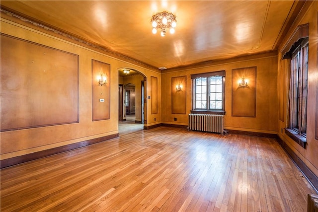 spare room featuring crown molding, radiator, hardwood / wood-style flooring, and arched walkways