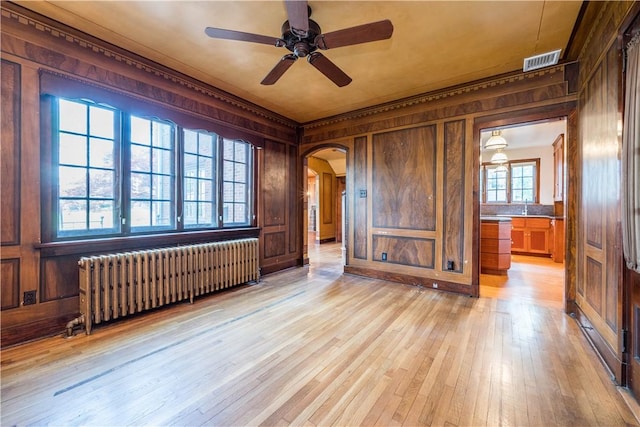 spare room with ceiling fan, visible vents, light wood-type flooring, wood walls, and radiator